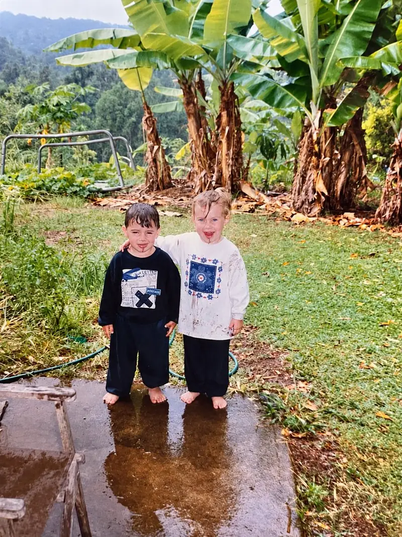 Emilee and Toby as toddlers, barefoot and grinning on the farm, banana plants behind them